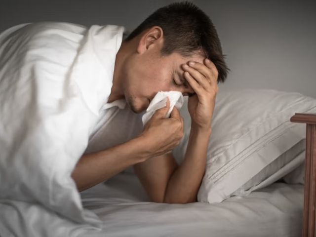 Image of Sick Man in Bed Blowing Nose